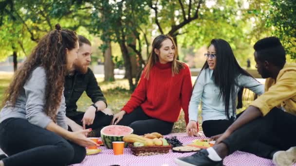 Zeitlupe attraktiver Mädchen, die kaukasisch und asiatisch reden, dann High-Five machen und beim Picknick im Herbst auf Plaid im Park lachen. Freizeit- und Freundschaftskonzept. — Stockvideo