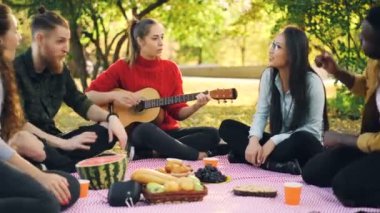 Romantik Genç insanlar şarkı ve ekose Park'ın bahçesinde oturan ve having fun pikniğe gitar çalmak vardır. Müzik aletleri ve kültür kavramı.