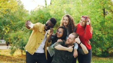 Neşeli gençlik erkekler ve kadınlar selfie smartphone kullanarak, komik surat ve açık havada duran ve gülen güneş gözlüğü takıyor parkta alıyor. Eğlenceli ve doğa kavramı.