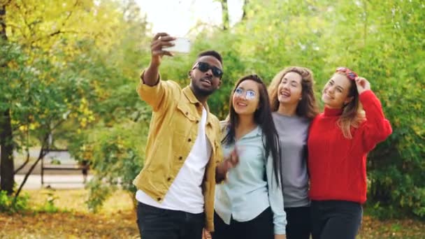 Estudante afro-americano está tirando selfie com meninas bonitas asiático e caucasiano de pé no parque, usando smartphone e posando para câmera. Conceito de juventude e foto . — Vídeo de Stock