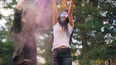 Ağır çekim güzel mutlu çift Asyalı kız ve Holi festival dans ve renkli boya park komik geleneğinde zevk atma beyaz adam.