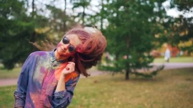 Ağır çekim portre sevimli genç kadın kaygısız öğrencinin saçını savurma Holi Festivali eğleniyor renkli toz ayakta dışında Park ile yalnız boyalı.