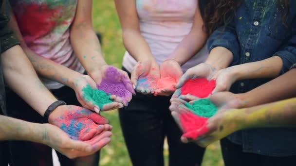 Slow motion of human hands holding multicolor powder paint gulal for Holi festival ceremony standing outside on lawn. People, fun and celebration concept. — Stock Video