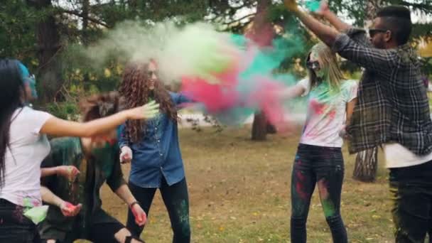 Rallentatore di studenti felici che si lanciano vernice colorata in polvere al festival di Holi ridendo e divertendosi godendo della gioiosa tradizione all'aperto nel parco . — Video Stock
