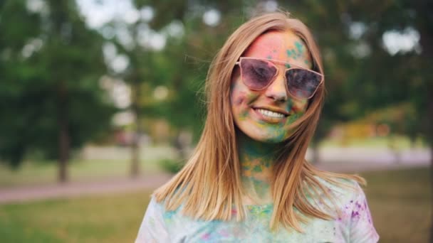 Slow motion portrait of happy girl with dirty face and T-shirt standing at Holi festival looking at camera and smiling enjoying Indian tradition. People and culture concept. — Stock Video