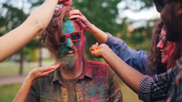 Lassú mozgás a halál szakállas fickó arc és a haj többszínű por festékkel Holi party szabadban diákok, fiatal férfi napszemüveg nevetve. — Stock videók