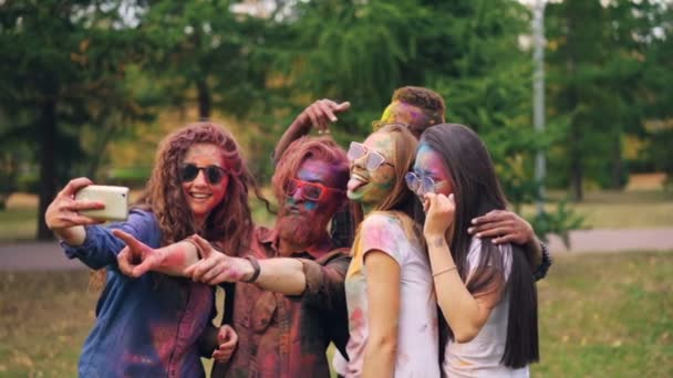 Šťastný, že muži a ženy přátelé s pomalované tváře a vlasy jsou při selfie na Holi festival pomocí smartphone fotoaparát, lidé jsou pózuje a usmíval se. Koncept zábavy a technologie. — Stock video