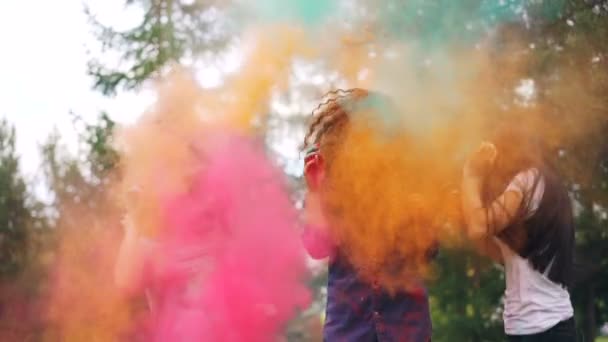 Chicas alegres se están divirtiendo bailando y riendo en las nubes de pintura en polvo en el festival Holi vistiendo ropa de moda manchada con pintura. Concepto de juventud y felicidad . — Vídeo de stock