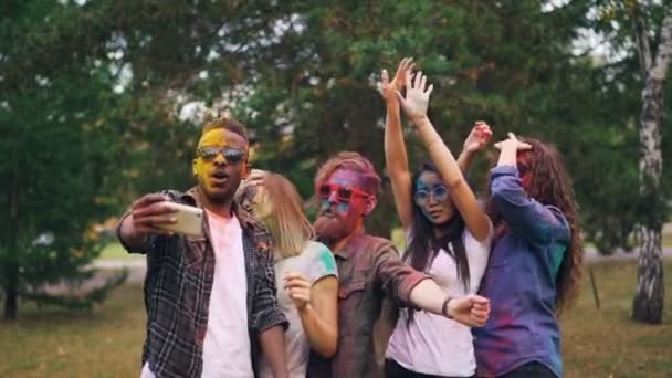 Slow motion av glada ungdomar i solglasögon med smutsiga ansikten och hår dansar och skrattar inspelning video på smartphone på part tar selfie. — Stockvideo
