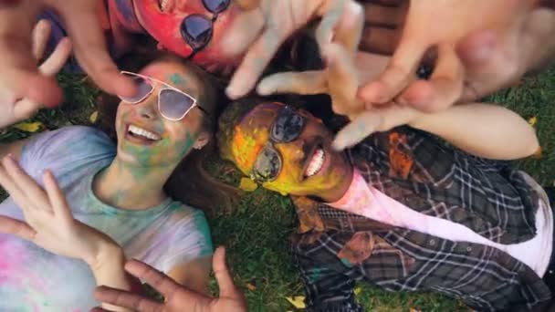 Zoom em câmera lenta de homens e mulheres deliciosos com rostos coloridos e roupas deitadas no gramado e mãos móveis se divertindo ao ar livre no festival Holi . — Vídeo de Stock