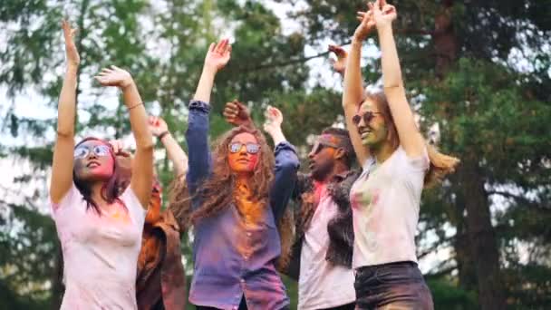 Glada män och kvinnor dansar ha kul på moderna fest, deras ansikten och kläder är täckt med multicolor färg. Festivaler, människor och natur koncept. — Stockvideo
