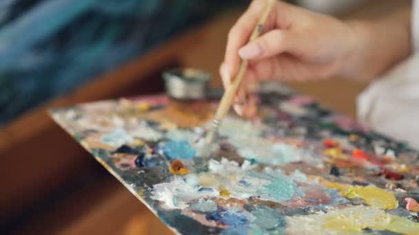 Gros plan d'une femme sale tenant un pinceau à la main et mélangeant les couleurs sur une palette, puis peignant un paysage marin sur toile. Art et outils concept . — Video