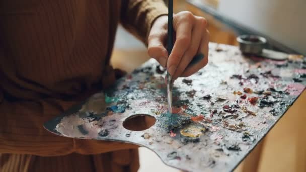 Close-up shot talentované ženy drží stopu a míchání barev na paletě pak Malování květy ve světlých olejovými barvami. Koncept kreativity, hobby a umění.
