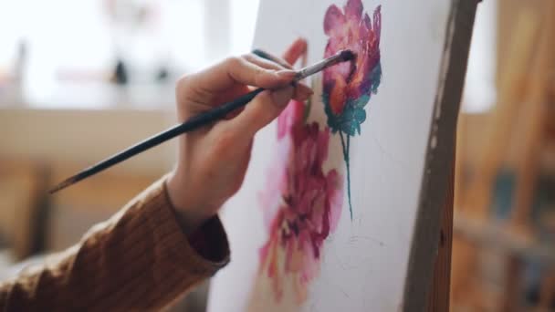 Close-up shot van vrouwelijke hand met penseel en schilderij heldere bloemen op canvas in lichte studio. Beeldende kunst, artistiek werk en mensen concept. — Stockvideo