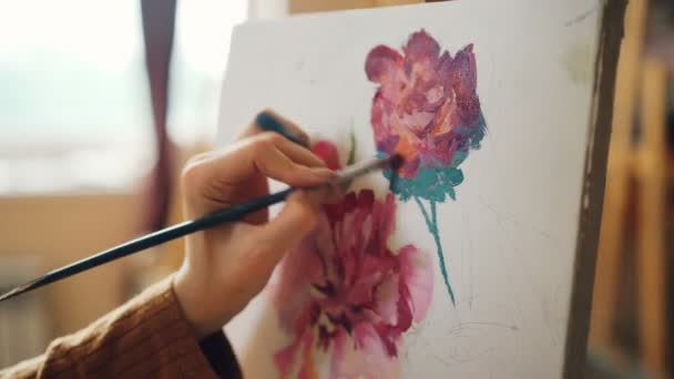 Nauwe schot van vuile meisjes hand bedrijf borstel en schilderij bloemen mooi stilleven foto in atelier alleen werken. Creativiteit en kunst concept. — Stockvideo