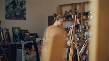 Yaratıcı genç bayan yağlı boya arka planda güzel sanat eserleri ile studio tek başına ayakta şövale önünde çalışma ile boyama. Hobi ve iş kavramı.