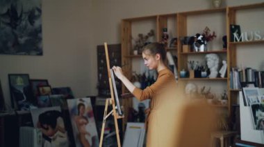 Sanat öğrencisi studio tek başına boyama resmi yağlı boya fırça kullanarak çalışıyor ve palet ayakta çalışma şövale yakınındaki çalışmalarına konsantre.