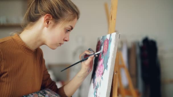 Ijverig kunst student mooi meisje is schilderen mooie foto bloemen werken in klasse staande in de buurt van ezel. Persoon is geconcentreerd op het creëren van illustraties. — Stockvideo