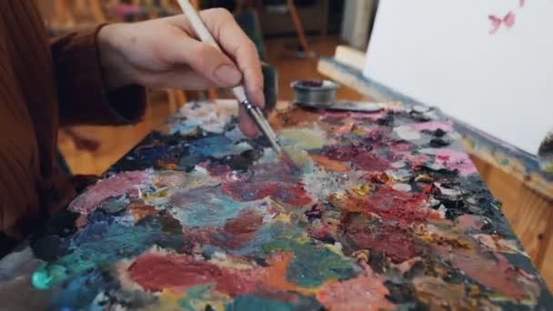 才能のある芸術の学生は 彼女のプロの女性教師が彼女の作品を見て キャンバスの上に花を絵画パレット上の色を混ぜています 創造性と教育の概念 — ストック動画