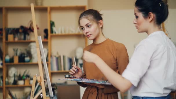 Artista hábil profesor experimentado está hablando con su estudiante enseñándole y explicándole cómo pintar, chica está escuchando y aprendiendo con sonrisa feliz . — Vídeos de Stock