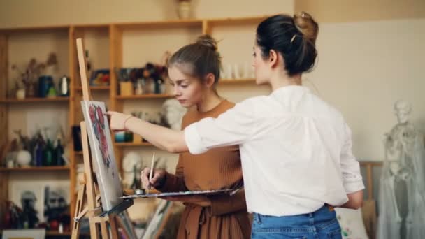 美丽的年轻女艺术家正在教她的学生画鲜花工作在工作室与油画和调色板 视觉艺术与创意青年理念 — 图库视频影像