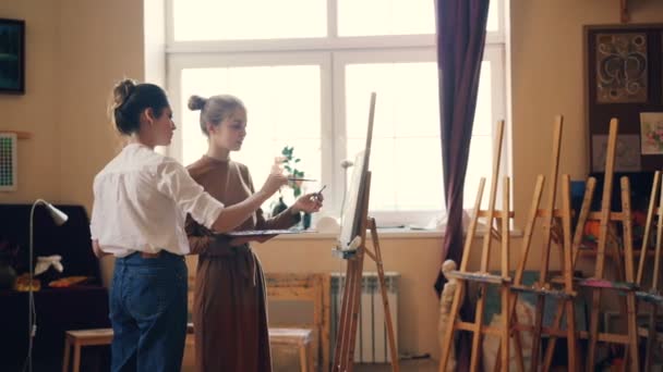 Hermosas jóvenes estudiantes y artistas profesionales están pintando juntas en el taller, la maestra está compartiendo experiencia y dando consejos. Concepto de arte y creatividad . — Vídeo de stock