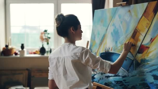 Artista femenina seria está trabajando en la imagen utilizando pinturas al óleo y paleta-cuchillo creando hermoso paisaje marino sobre lienzo. Técnica de pintura y concepto de pintores . — Vídeos de Stock