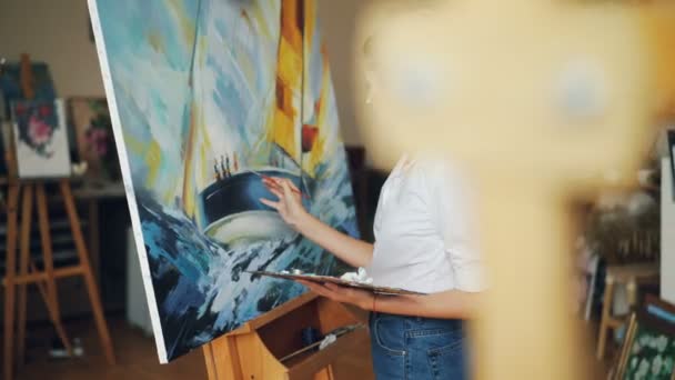 Artista femenina se concentra en el trabajo de pintura hermosa imagen de mar y barco con pinturas al óleo que trabajan solos en el estudio utilizando colores brillantes. Concepto de arte y creatividad . — Vídeos de Stock
