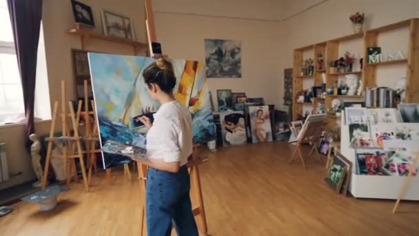 Panera de niña profesional pintor serio que trabaja en la pintura de estudio paisaje marino con pinturas tempera celebración de la paleta y el pincel. Obras de arte y concepto de creatividad . — Vídeos de Stock