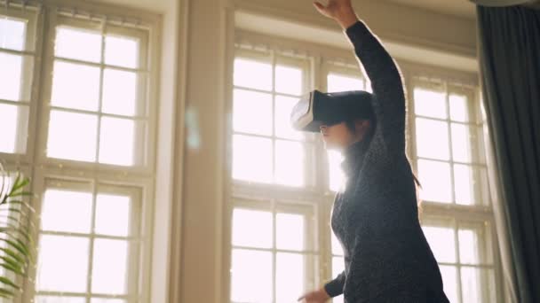 Jovencita está disfrutando de una nueva experiencia en gafas de realidad virtual en movimiento brazos y cuerpo de pie en la habitación con gafas ar. Ventana panorámica está en el fondo . — Vídeos de Stock