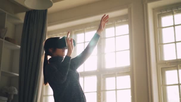 Jeune brune utilise des lunettes de réalité augmentée à la maison en déplaçant les mains et le corps debout dans la chambre seule en profitant de la technologie moderne et du divertissement . — Video