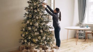 İnce genç bayan parlak topları dokunmadan yılbaşı ağacı süsleme ve kapalı evde tek başına ayakta ışıklar. Noel süslemeleri, iç ve insanlar kavramı.