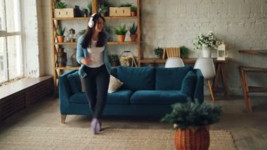 Neşeli genç kadın ev eğleniyor ve serbest zaman zevk kulaklık üzerinden müzik dinleme dans ediyor. Modern room-loft tarzı iç görülür.