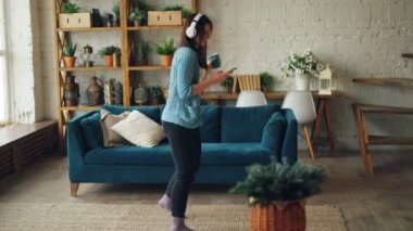 Mutlu genç kadın evde kupa ve smartphone ücretsiz vaktinizi kulaklık ile müzik ile dans ediyor. Gençlik Kültür ve yaşam tarzı kavramı.