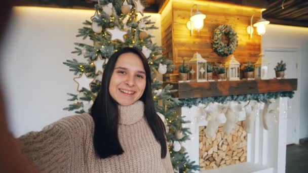 Punto de vista de la foto de la guapa morena tomando selfie el día de Navidad sosteniendo la cámara y posando con gestos de mano y caja de regalo expresando emociones positivas . — Vídeo de stock