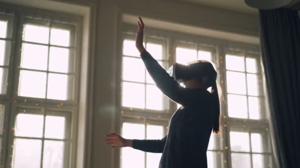 Mulher jovem está usando óculos de realidade virtual dentro de casa com grande janela panorâmica no fundo. Tecnologia moderna, entretenimento e conceito de pessoas . — Vídeo de Stock