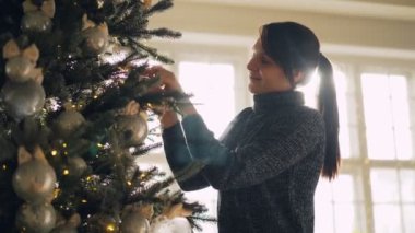 Gülümseyen öğrenci gümüş top asılı yapay yılbaşı ağacı süsleme ve Noel tatili için hazırlanıyor dalları dokunmadan ışıklar. Kutlamalar ve şenlikli iç kavramı.