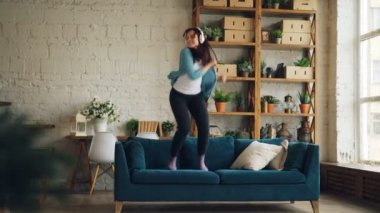 Oynak kız ev kulaklık üzerinden müzik, kanepenin üzerinde dans ve yastık atma, eğleniyor. Eğlence, insanlar ve yaşam tarzı kavramı.