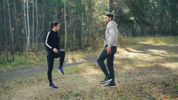 Gelukkige paar uitoefent in park doen warming-up activiteiten glimlachend en praten genieten van frisse lucht en een gezonde levensstijl. Jeugd, ontspanning en recreatie concept. — Stockvideo