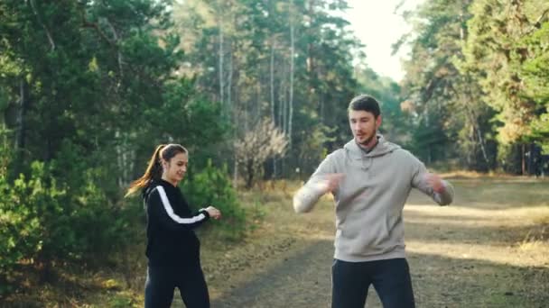 Bella coppia si sta godendo l'allenamento all'aperto nel parco facendo esercizi e sorridendo insieme indossando abbigliamento sportivo. Millennials, benessere e concetto di natura . — Video Stock