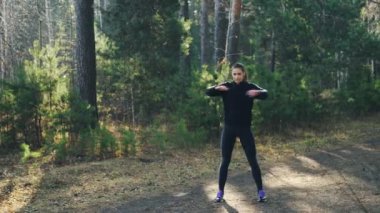 Modern eşofman yakışıklı genç kadın tek başına park ısınma-up silah ve yoldaki ağaçları arasında ayakta vücut kasları egzersiz olduğunu. Gençlik ve spor genel kavram.