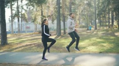 Yan görünümü çalışan ve birlikte sonbahar günü sıcak güneşli yolda üzerinde atlama Park spor yapan adam ve yakışıklı genç insanlar kız. Doğa ve etkinlik kavramı.