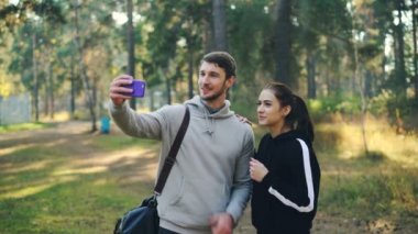 Çekici kadın ve adam online video seslenmek ile smartphone parkta sonra spor eğitim yapıyoruz. Adam mermiyi tutuyor olabilir, eller, konuşan ve gülen insanlar sallayarak.