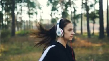 Güzel genç bayan kulaklıklar giyen ve müzik zevk etkinliği ve en sevdiğiniz şarkı dinlemek ve gülümseyen Park'ta jogging. Doğa, gençlik ve teknoloji kavramı.