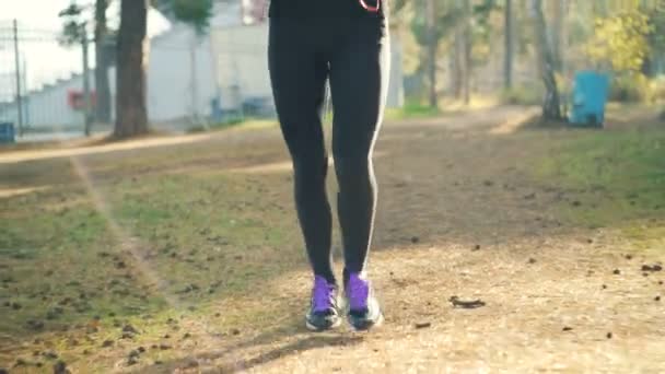 Incline-se tiro de menina bonita em treinadores e traje de treino correndo no parque usando fones de ouvido e desfrutando de atividade física e natureza. Pessoas e conceito de esportes . — Vídeo de Stock