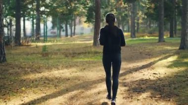 Arkadan görünüşü Park'ta jogging ve müzik eğitim yalnız dinlerken kulaklık giyen spor giyim ince genç kadın. Alt, spor ve doğa kavramı.