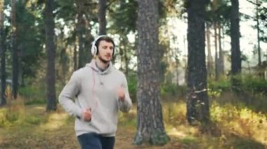 Yakışıklı genç adam parkta koşu ve şarkı ve fiziksel aktivite zevk kulaklık üzerinden müzik Dolly vurdu. Gençlik Kültür ve spor kavramı.