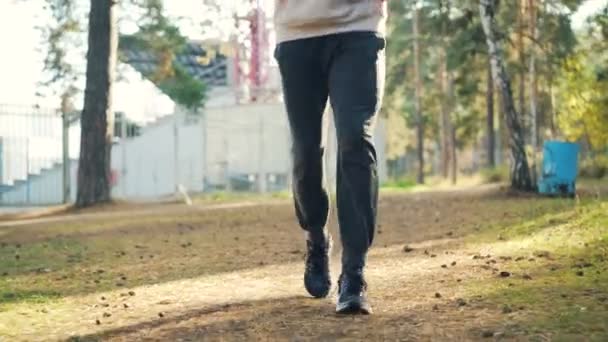 Tilt-up shot van knappe jongen in trainers en trainingspak joggen in park hoofdtelefoon dragen en genieten van lichaamsbeweging en herfst aard. Mensen en sport concept. — Stockvideo