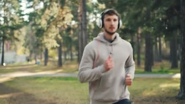 Aantrekkelijke man in trendy sweatshirt draait in park hoofdtelefoon dragen en het luisteren naar de radio alleen op zomerdag. Mensen, technologie en hobby concept. — Stockvideo