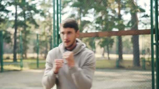 Actieve jonge man in sweatshirt doet sport in park boksen alleen in recreatiegebied bewegende armen op zomerdag. Gezonde lifestyle, hobby en mensen concept. — Stockvideo